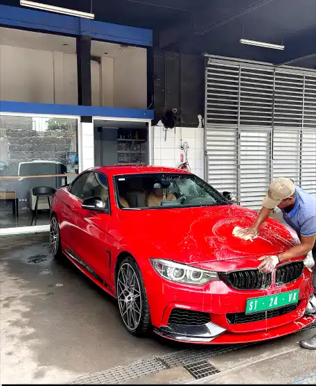 Mão a lavar um carro azul com uma esponja coberta de espuma